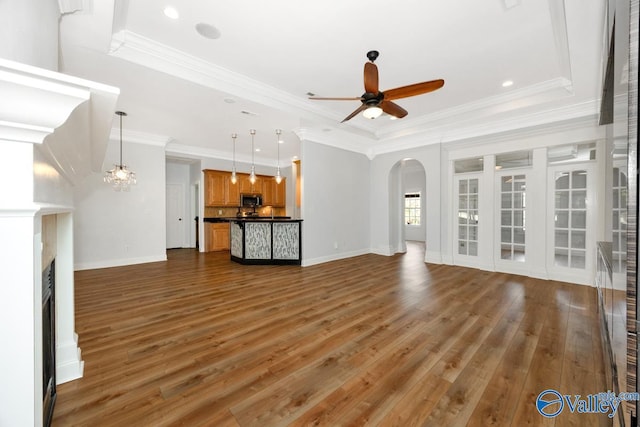 unfurnished living room with ceiling fan, arched walkways, a fireplace, baseboards, and a raised ceiling