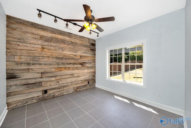 spare room with ceiling fan, baseboards, dark tile patterned floors, and wooden walls
