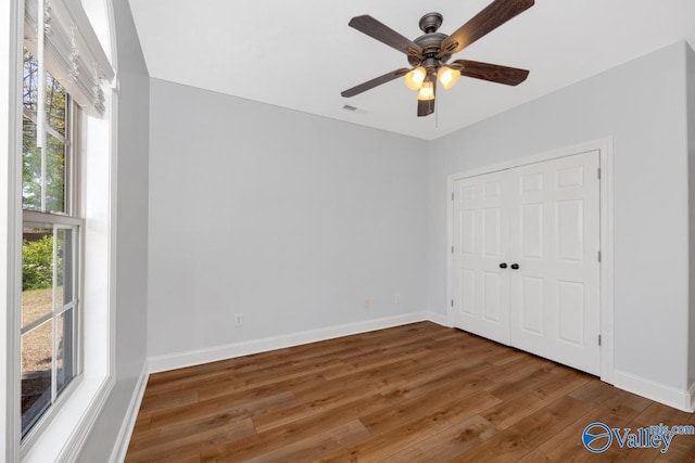 unfurnished bedroom with baseboards, wood finished floors, a closet, and multiple windows