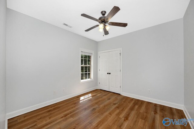 empty room featuring wood finished floors, visible vents, baseboards, and ceiling fan
