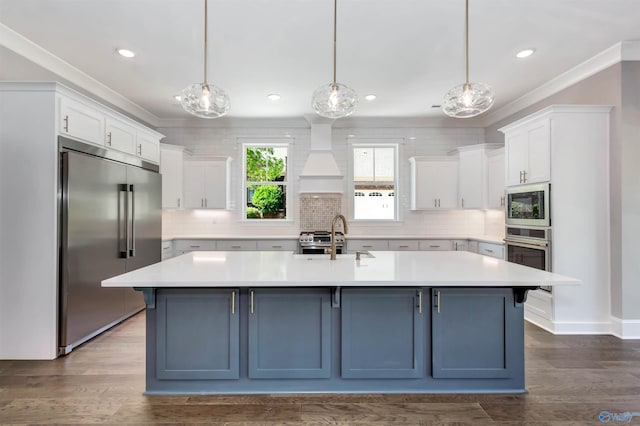 kitchen featuring built in appliances, pendant lighting, and a center island with sink