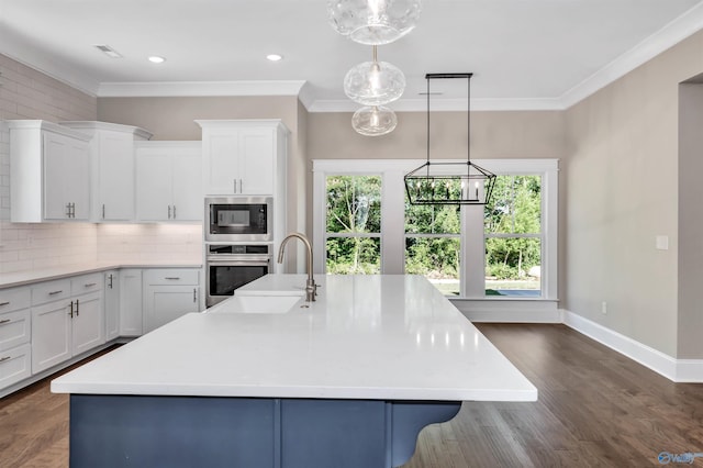 kitchen with oven, built in microwave, white cabinets, hanging light fixtures, and a kitchen island with sink