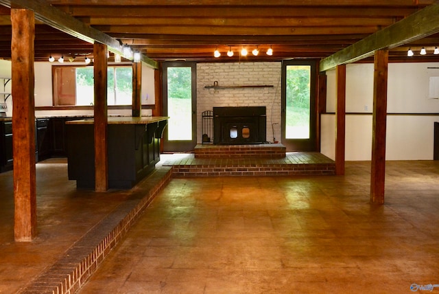 unfurnished living room with beamed ceiling, rail lighting, a brick fireplace, tile patterned floors, and brick wall