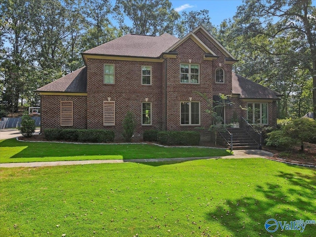 colonial home featuring a shingled roof, a front lawn, and brick siding