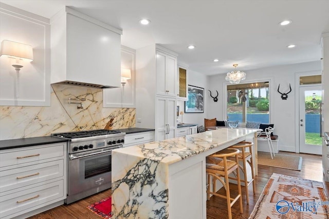 kitchen with dark wood-style floors, a breakfast bar, high end stainless steel range, tasteful backsplash, and white cabinets