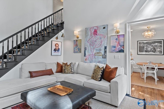 living area with a high ceiling, stairway, wood finished floors, and an inviting chandelier