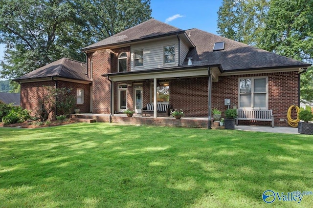 back of house with covered porch, roof with shingles, a lawn, and brick siding