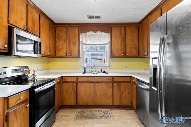 kitchen with sink, a textured ceiling, light hardwood / wood-style flooring, and appliances with stainless steel finishes