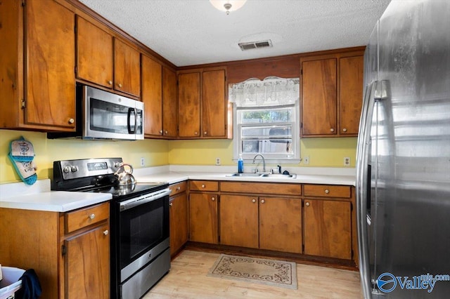 kitchen with sink, light wood-type flooring, a textured ceiling, and stainless steel appliances