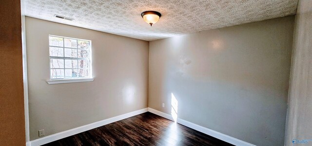 empty room with baseboards, a textured ceiling, visible vents, and dark wood-type flooring