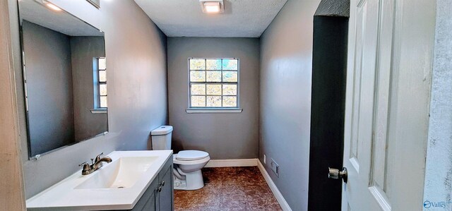 half bath with baseboards, vanity, toilet, and a textured ceiling