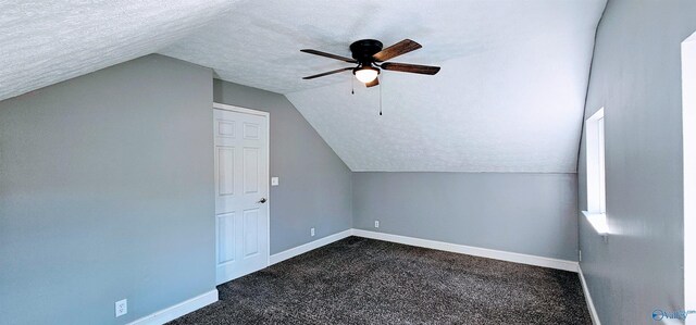 additional living space with a textured ceiling, dark carpet, lofted ceiling, and baseboards