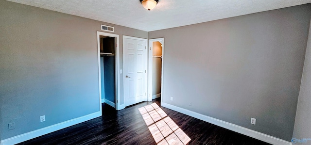 unfurnished bedroom featuring a textured ceiling, visible vents, baseboards, a closet, and dark wood-style floors