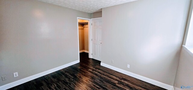 unfurnished room with a textured ceiling, dark wood-type flooring, and baseboards