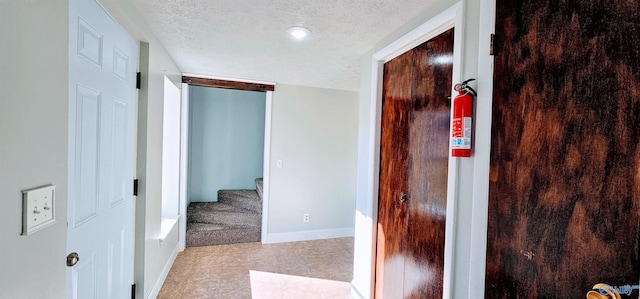 hallway featuring a textured ceiling, stairs, and baseboards