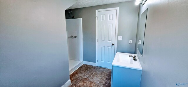 full bath with a textured ceiling, walk in shower, vanity, and baseboards