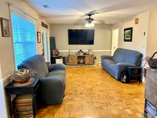 living room featuring ceiling fan, light parquet floors, and a textured ceiling