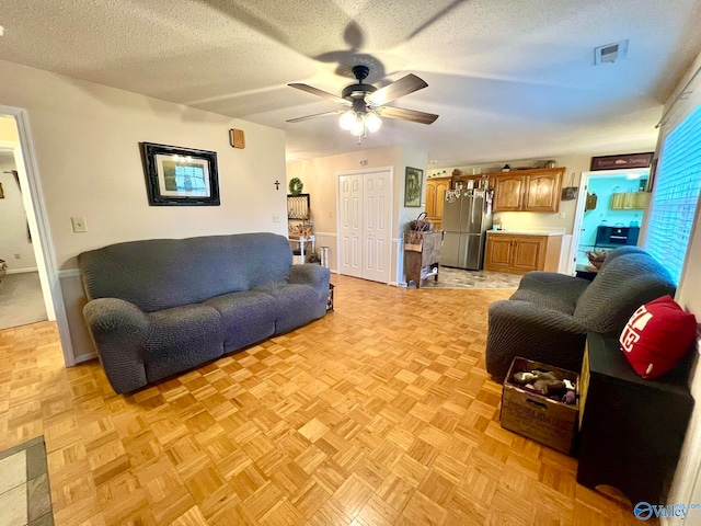 living room featuring ceiling fan, a textured ceiling, and light parquet floors