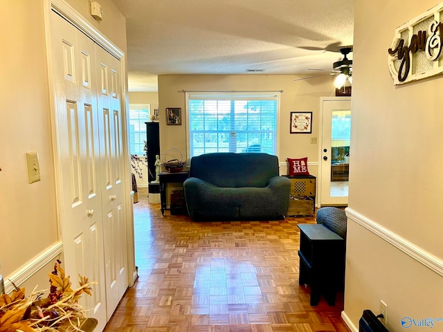 living room with ceiling fan, a textured ceiling, and light parquet floors