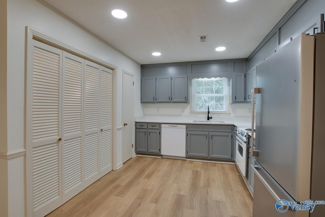 kitchen with visible vents, light wood-type flooring, gray cabinets, white appliances, and a sink