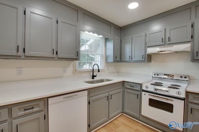 kitchen featuring under cabinet range hood, light countertops, gray cabinets, white appliances, and a sink