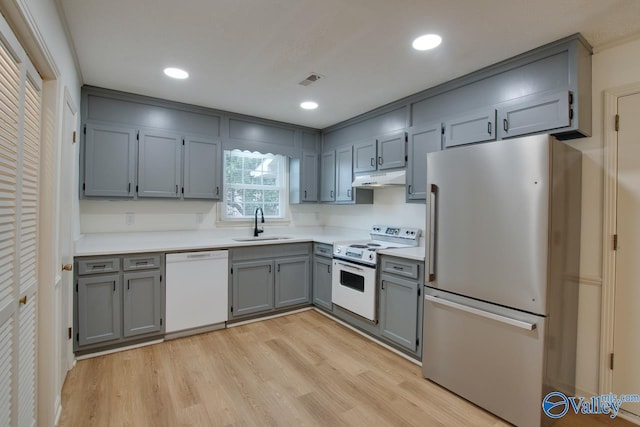 kitchen featuring gray cabinetry, under cabinet range hood, a sink, white appliances, and light wood-style floors