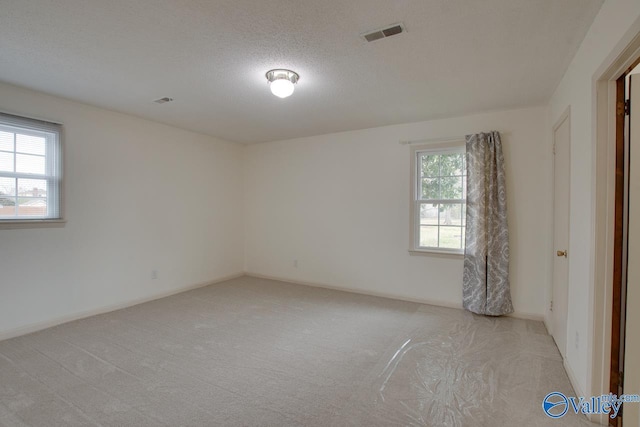 spare room featuring visible vents, light carpet, a textured ceiling, and baseboards