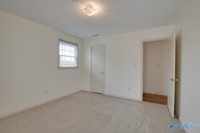 unfurnished bedroom with visible vents, light colored carpet, a textured ceiling, and baseboards