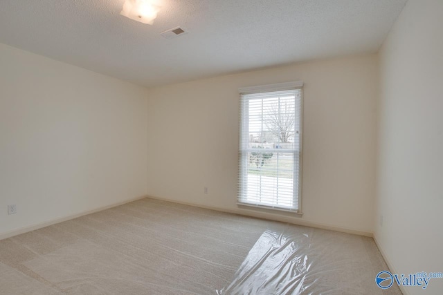 spare room featuring visible vents, light colored carpet, a textured ceiling, and baseboards