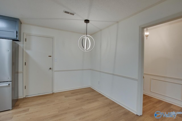 unfurnished dining area with light wood finished floors, visible vents, a textured ceiling, and a wainscoted wall