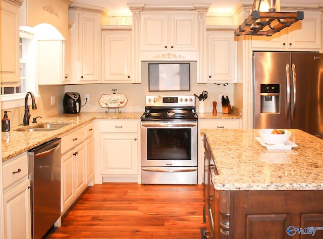 kitchen with light wood-type flooring, light stone counters, sink, appliances with stainless steel finishes, and ornamental molding