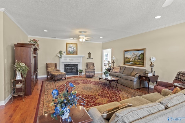 living room with a tile fireplace, ornamental molding, wood-type flooring, and a textured ceiling