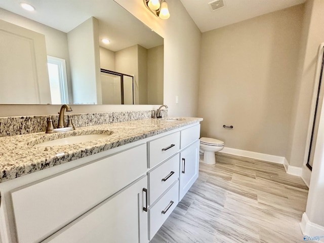 bathroom featuring hardwood / wood-style floors, vanity, a shower with shower door, and toilet