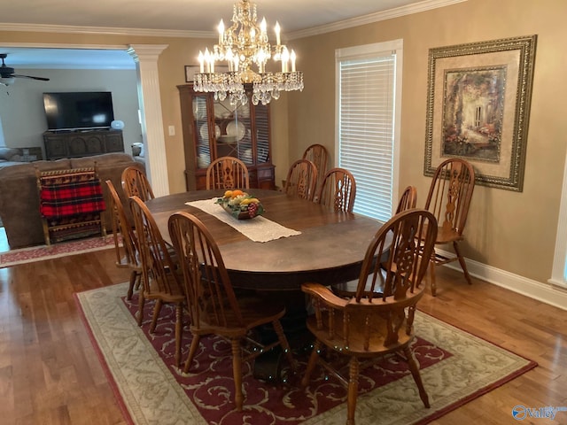 dining space with wood-type flooring, ceiling fan with notable chandelier, ornate columns, and ornamental molding