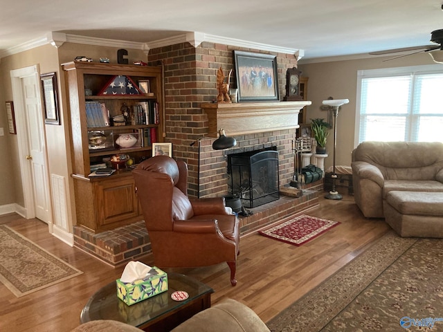 living room with hardwood / wood-style floors, ceiling fan, crown molding, and a brick fireplace