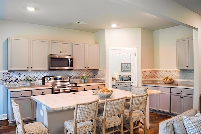 117 Edensmith Dr, New Market, AL 35761 - kitchen with appliances with stainless steel finishes, a kitchen bar, decorative backsplash, dark wood-style floors, and an island with sink