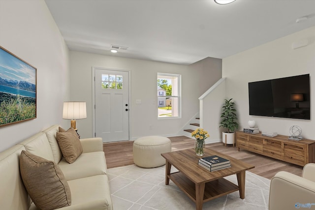 living area with light wood-style flooring, stairs, visible vents, and baseboards