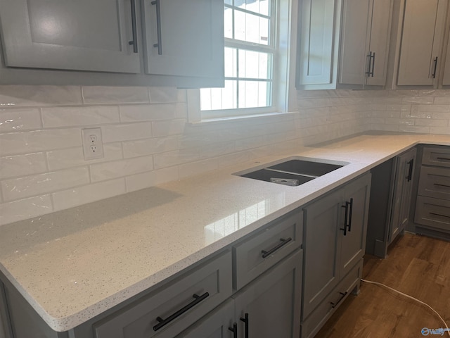 kitchen with light stone counters, gray cabinetry, a sink, tasteful backsplash, and dark wood finished floors