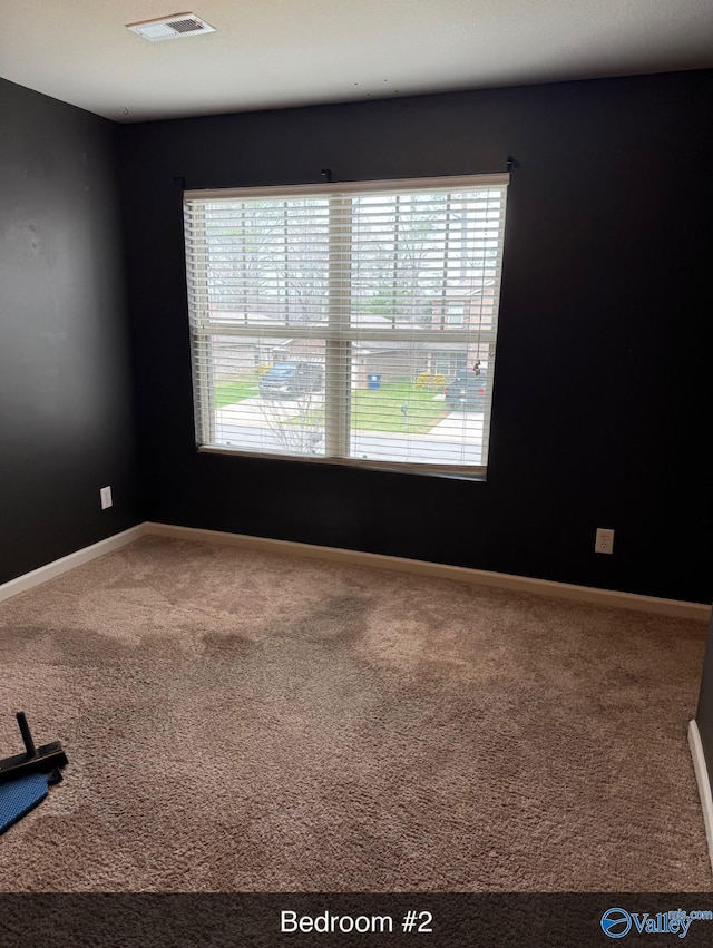empty room featuring carpet, visible vents, and baseboards