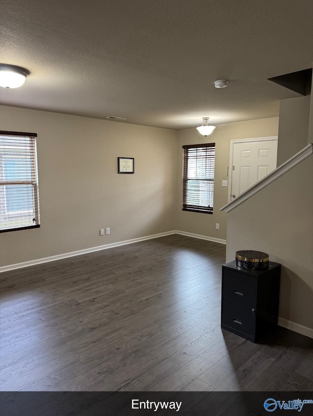 unfurnished living room with visible vents, dark wood-type flooring, a textured ceiling, stairway, and baseboards