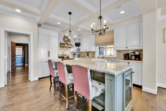 kitchen with a kitchen island, under cabinet range hood, stainless steel range with electric cooktop, white cabinetry, and a sink