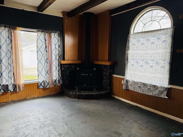 unfurnished living room with a wainscoted wall, beam ceiling, wood walls, and a wood stove