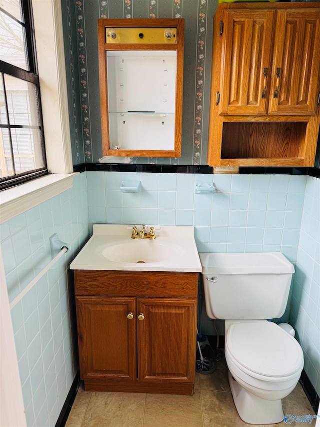 bathroom featuring toilet, tile walls, vanity, wainscoting, and tile patterned floors