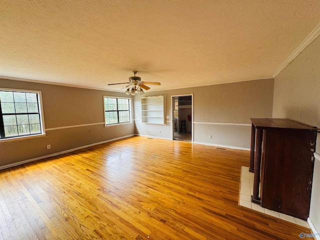 empty room featuring hardwood / wood-style flooring, built in shelves, ornamental molding, and a textured ceiling