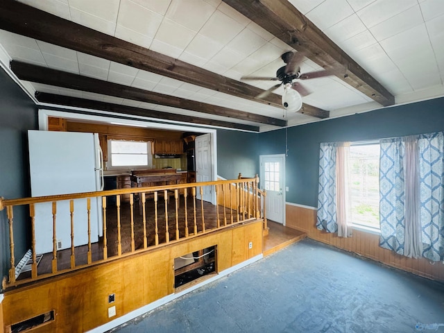 spare room with beam ceiling, a wainscoted wall, ceiling fan, wooden walls, and concrete floors