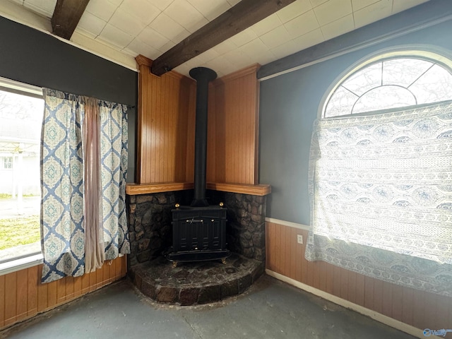 room details featuring wood walls, wainscoting, beam ceiling, unfinished concrete flooring, and a wood stove