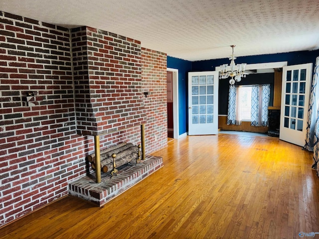 unfurnished living room with a chandelier, brick wall, a textured ceiling, and wood-type flooring