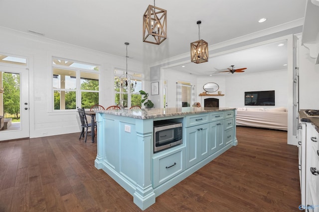 kitchen featuring pendant lighting, stainless steel microwave, open floor plan, a kitchen island, and light stone countertops