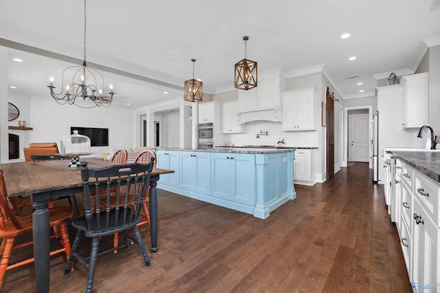 kitchen with white cabinets, dark countertops, open floor plan, a fireplace, and pendant lighting