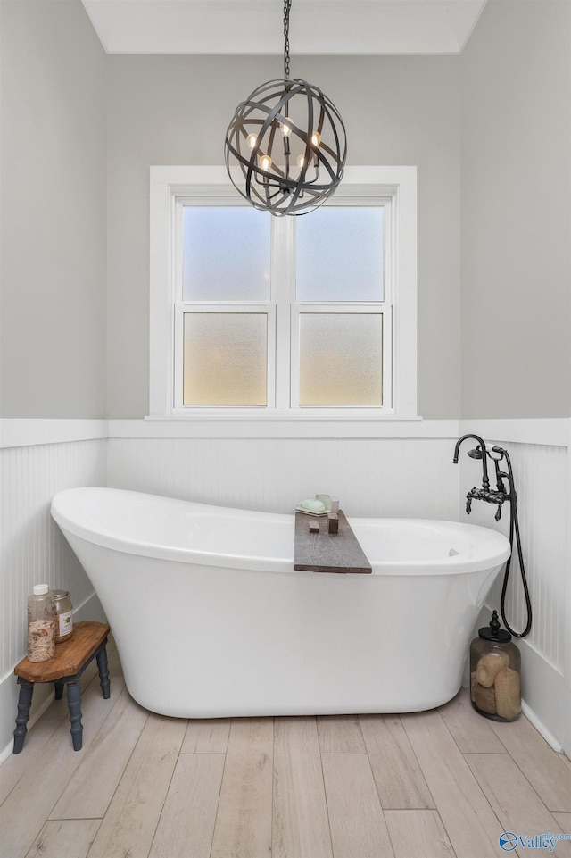 full bath featuring a healthy amount of sunlight, a soaking tub, a wainscoted wall, and wood finished floors